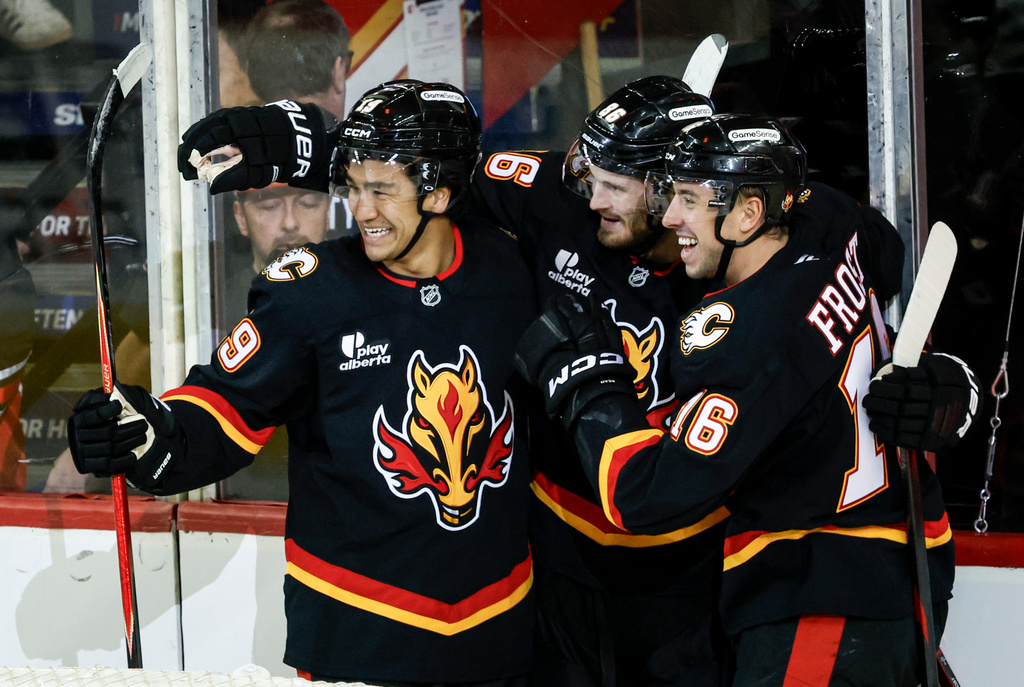 Calgary Flames' Joel Farabee, center, celebrates his goal with teammates Zayne Parekh, left, and Morgan Frost during the second period of an NHL hockey game against the Carolina Hurricanes in Calgary, Alberta, on Saturday, March 7, 2026. (Jeff McIntosh/The Canadian Press via AP)