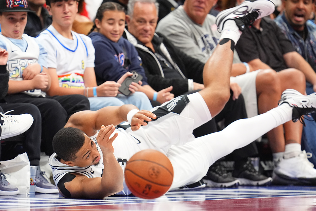 San Antonio Spurs guard Keldon Johnson slides into fans in the trying to save a ball from bouncing out of play in the first half of an NBA basketball game against the Denver Nuggets, Friday, Nov. 28, 2025, in Denver. (AP Photo/David Zalubowski)
