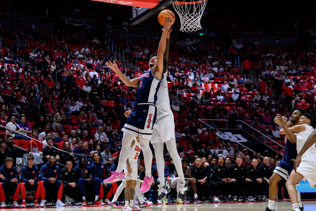 Arizona guard Brayden Burries, left, goes to the basket for a layup guarded by Utah forward Seydou Traore, center, during the second half of an NCAA college basketball game, Saturday, Jan. 3, 2026, in Salt Lake City. (AP Photo/Tyler Tate)