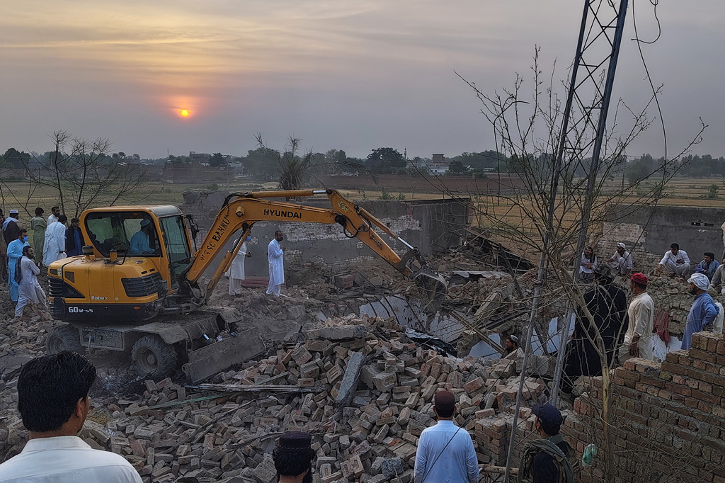A worker clear rubble with an excavator as a police officers and local residents gather at the site of overnight suicide bombing at a security post in Fatah Khel, in Bannu, a district in Pakistan's Khyber Pakhtunkhwa province bordering Afghanistan, Sunday, May 10, 2026. (AP Photo/Aamad Khattak)
