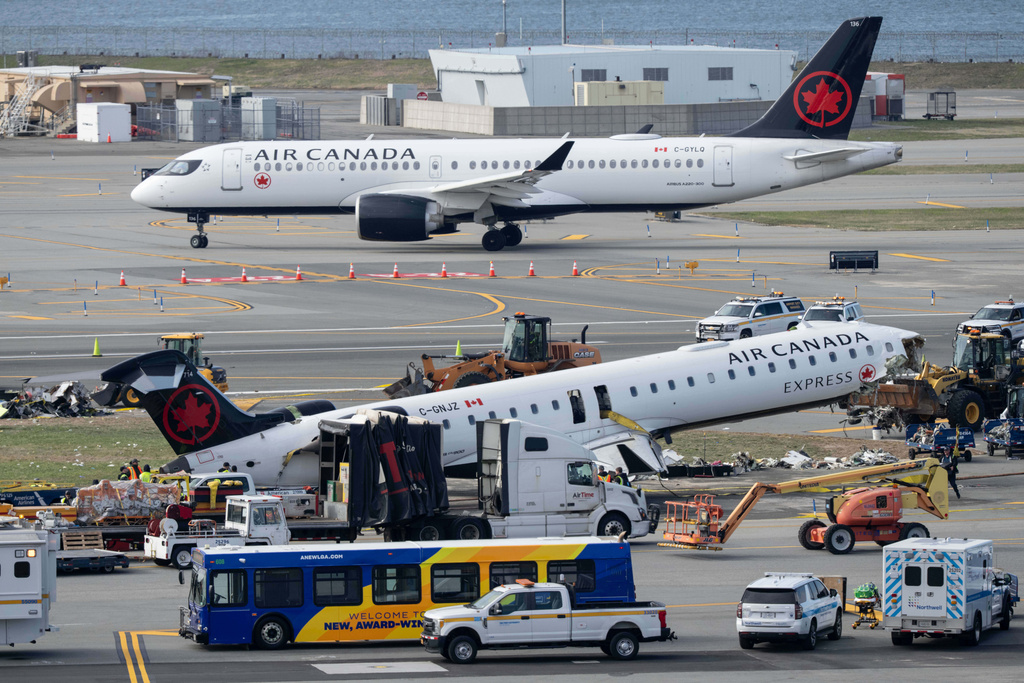 An Air Canada Express jet taxis past the wreckage of an Air Canada Express jet, Wednesday, March 25, 2026, as maintenance crews prepare to move the plane from the runway where it had collided with a Port Authority fire truck Sunday night at LaGuardia Airport, in New York. (AP Photo/Yuki Iwamura)