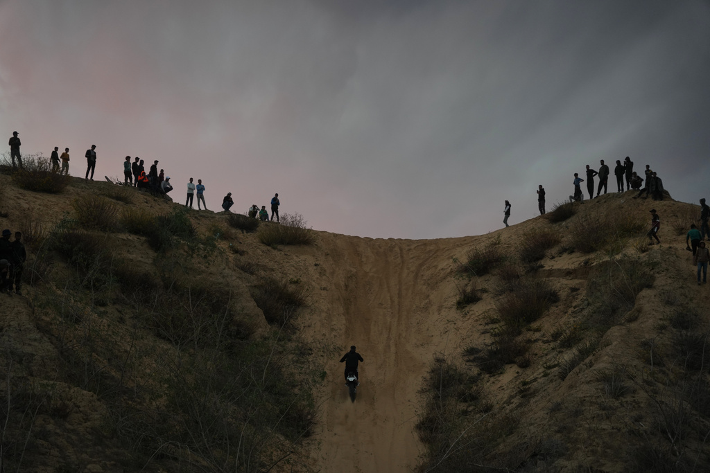 Palestinians watch youths riding their motorcycles on sand dunes in the Al-Zahra area, in the central Gaza Strip, Friday, Dec. 5, 2025. (AP Photo/Abdel Kareem Hana)