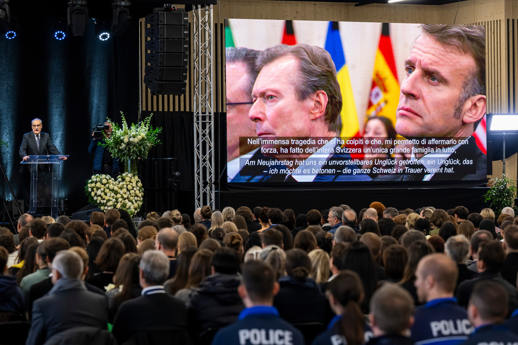 Swiss Federal President Guy Parmelin, left, delivers his statement as Former Grand Duke of Luxembourg Henri, left, and Emmanuel Macron, right, President of France appear on the screen, during the official commemorative ceremony for the victims of the deadly fire at the "Le Constellation" bar in Crans-Montana, in Martigny, Switzerland, Friday, Jan. 9, 2026. (Laurent Gillieron/Keystone/Pool via AP)