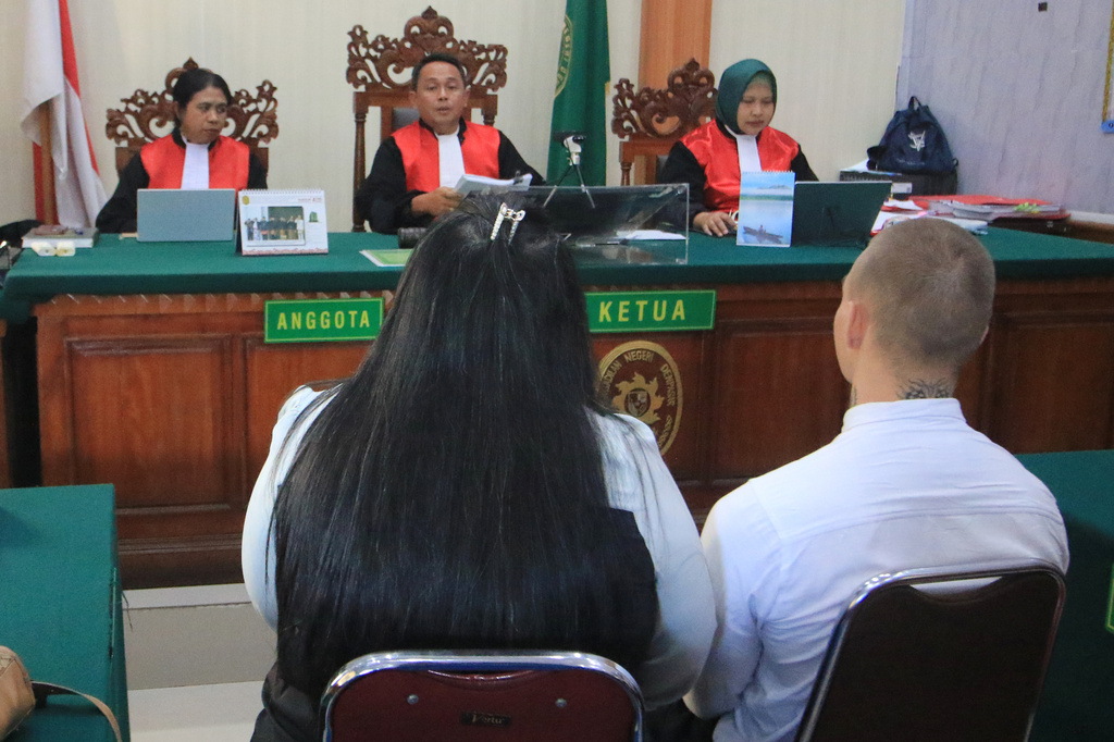 Swiss tourist Luzian Andrin Zgraggen, back to camera, right, who is accused of insulting the Balinese Hinduism's sacred Day of Silence in social media posts sits on the defendant's chair with an interpreter during his sentencing hearing at the district court in Denpasar, Bali, Indonesia, Thursday, Aug. 20, 2026. (AP Photo)