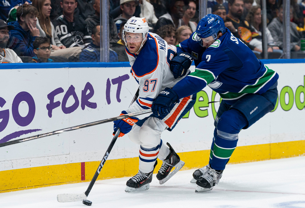 Vancouver Canucks' Luke Schenn (2) tries to check Edmonton Oilers' Connor McDavid (97) during second period NHL hockey action in Vancouver, B.C., on Thursday, Oct. 1, 2026. (Rich Lam/The Canadian Press via AP)