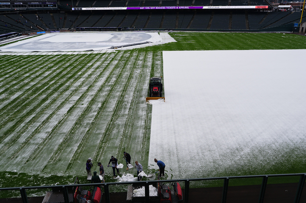 Grounds crew members toil to clear the outfield of Coors Field after a spring storm blanketed the intermountain West with a light covering of snow before the Colorado Rockies host the Los Angeles Dodgers in a baseball game Friday, April 17, 2026, in Denver. (AP Photo/David Zalubowski)
