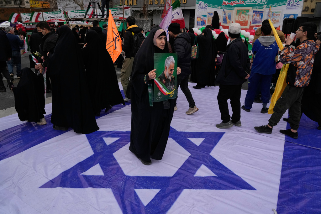 A woman holds a poster of the late commander of Iran's Revolutionary Guard expeditionary Quds Force, Gen. Qassem Soleimani, who was killed in a U.S. drone attack in 2020 in Iraq, as she stands on a banner containing an image of the Israeli flag in an annual rally marking 1979 Islamic Revolution at the Azadi, or Freedom, Street in Tehran, Iran, Wednesday, Feb. 11, 2026. (AP Photo/Vahid Salemi)