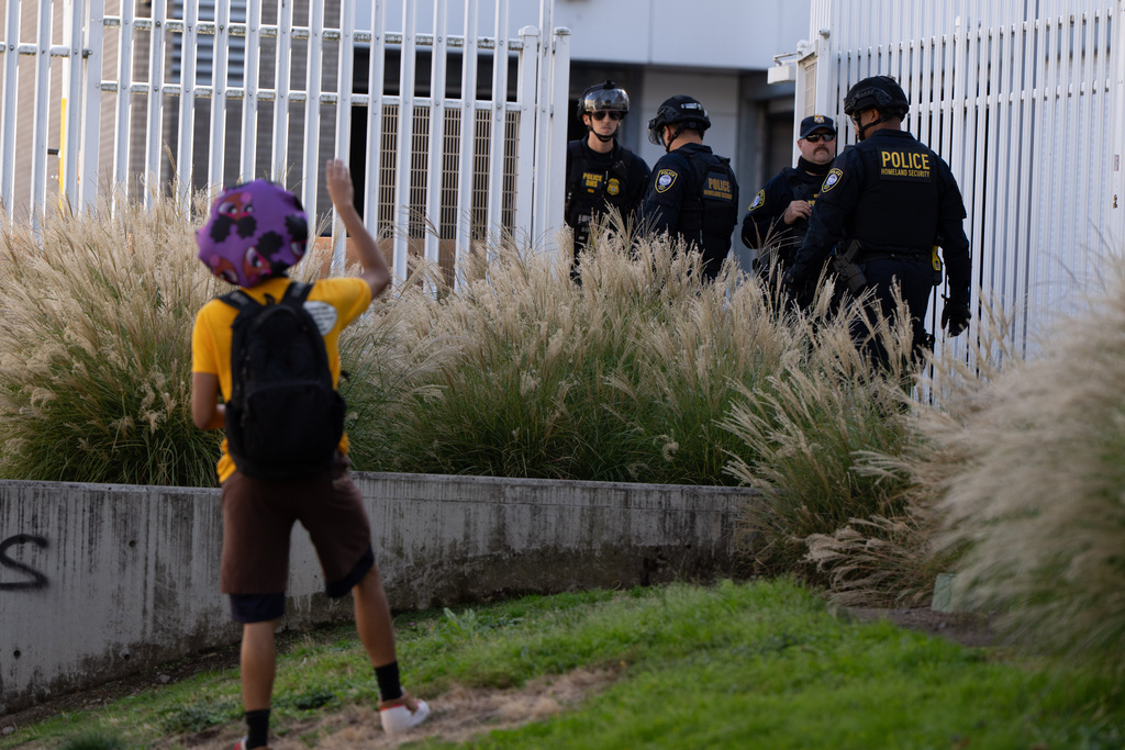 A protester waves to Department of Homeland Security officials as they walk to the gates of the U.S. Immigration and Customs Enforcement facility after inspecting an area outside on Sunday, Sept. 28, 2025, in Portland, Ore. (AP Photo/Jenny Kane)
