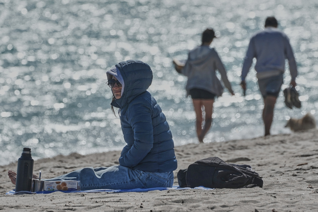 A bundled up Lucia Amato, of Argentina, sits on the shore while waiting for a friend in Miami Beach, Fla., Thursday, Jan. 29, 2026.A bundled up (AP Photo/Marta Lavandier)