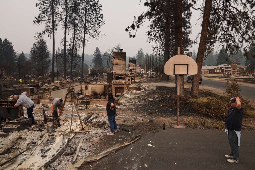 From left, homeowner Al Acosta, his son Louis Acosta, daughter Renee Stewart and son-in-law Jamie Stewart look through the remains of Al's home after a wildfire hit the northern part of Spokane, Wash., Monday, Aug. 3, 2026. (AP Photo/Lindsey Wasson)