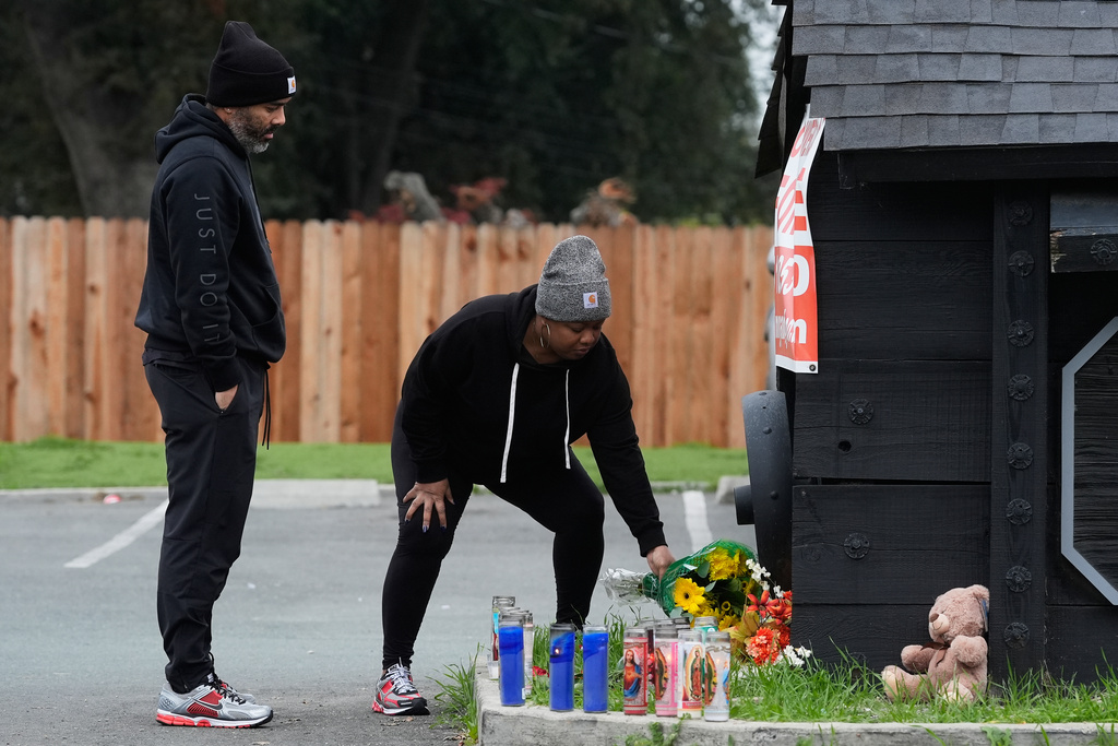 Aundre Smith, left, watches as Genesis Smith places flowers near the scene of a mass shooting on Saturday at a banquet hall in Stockton, Calif., Monday, Dec. 1, 2025. (AP Photo/Jeff Chiu)