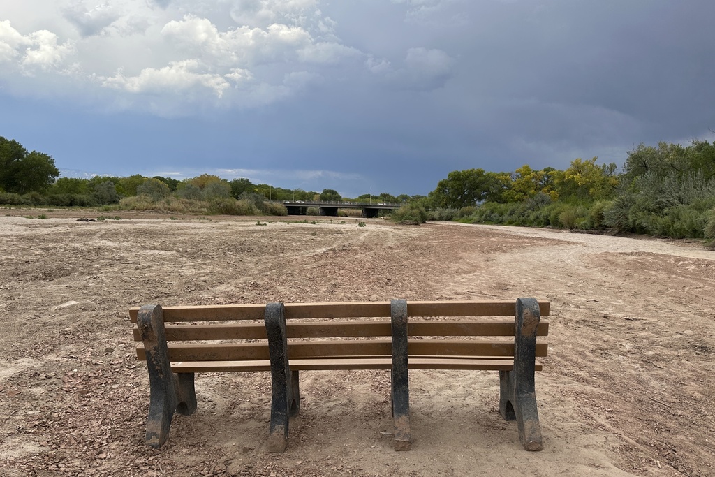 A park bench sits in the dry riverbed of the Rio Grande as traffic crosses a bridge along historic Route 66 in Albuquerque, N.M., on Thursday, Aug. 21, 2025. (AP Photo/Susan Montoya Bryan)