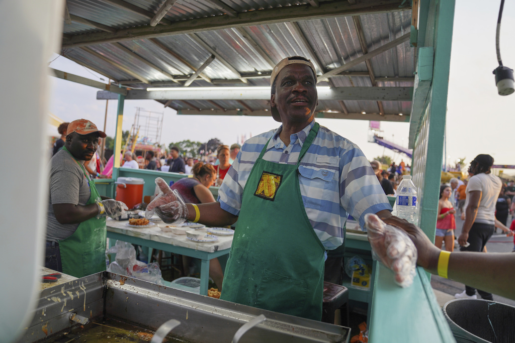 Bienvenue D'Almeida, who applied for and won the so-called green card lottery, a program for countries with low rates of emigration to the United States, makes funnel cake and deep-fried Snickers bars at the St. Jude Catholic Church's Sweet Corn Festival on Saturday, Aug. 9, 2025, in Cedar Rapids, Iowa. (AP Photo/Jessie Wardarski)