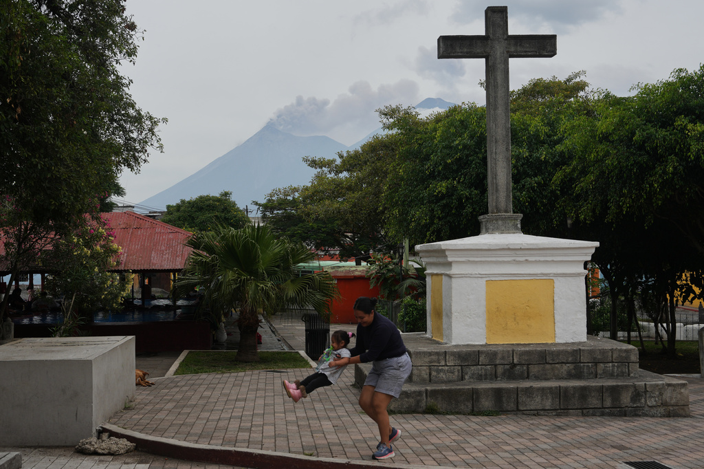 A woman playfully swings a child as clouds of ash rise from the crater of the Fuego volcano, as seen from San Pedro Las Huertas, Guatemala, Tuesday, Aug. 4, 2026. (AP Photo/Moises Castillo)