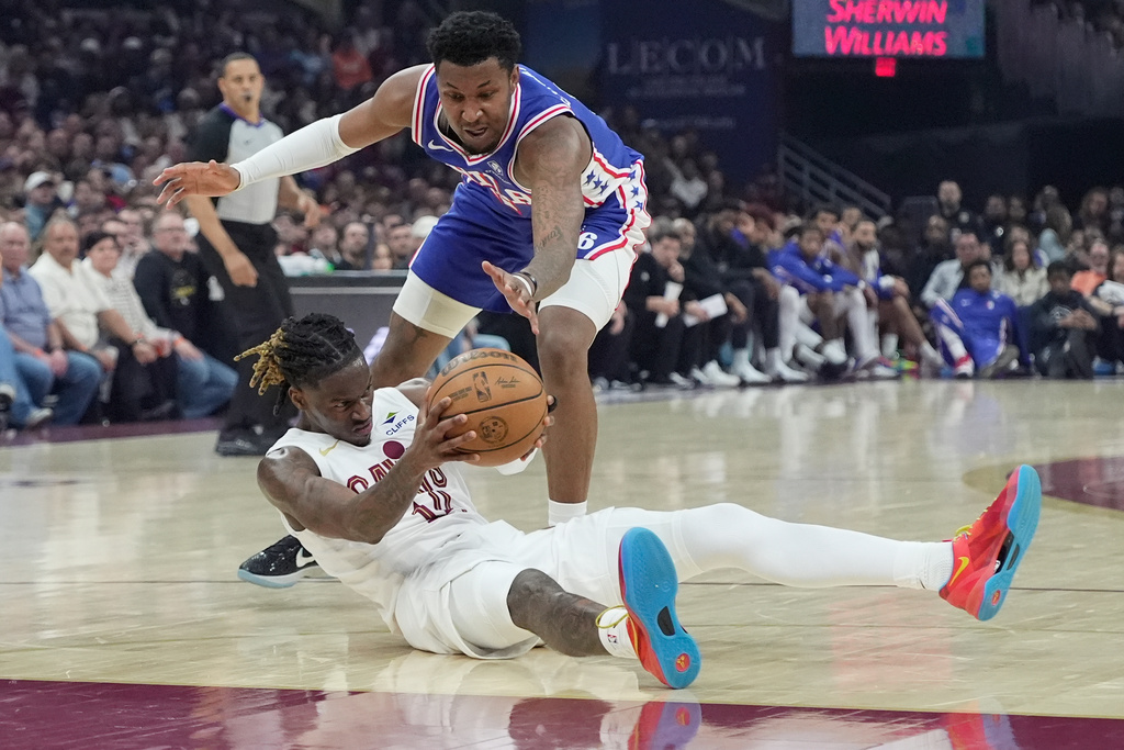 Philadelphia 76ers forward Justin Edwards, top, reaches for the ball held by Cleveland Cavaliers guard Keon Ellis, bottom, in the first half of an NBA basketball game in Cleveland, Monday, March 9, 2026. (AP Photo/Sue Ogrocki)