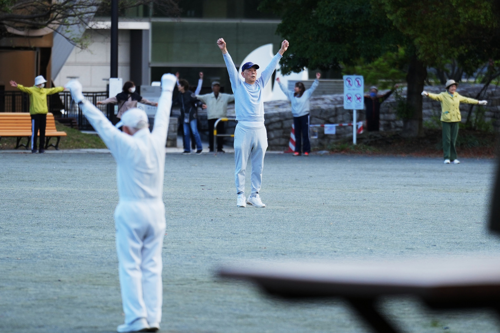 People perform a stretching exercise while listening to music and guidance from radio at a public park in Tokyo, Monday, April 6, 2026. (AP Photo/Hiro Komae)