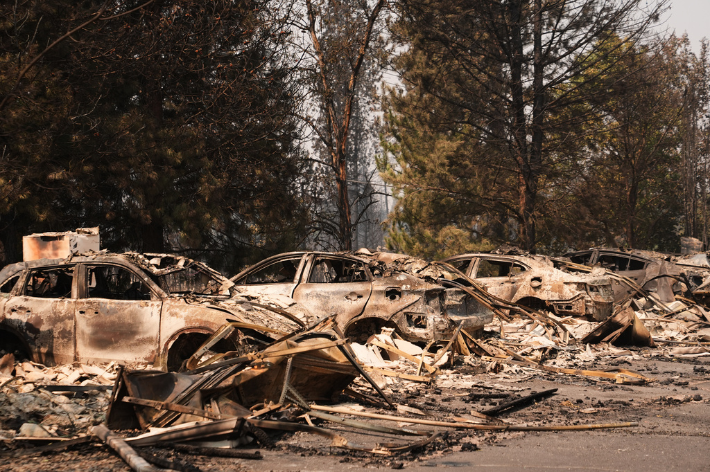 A line of burned cars sit in a parking lot Tuesday, Aug. 4, 2026, after a wildfire hit the northern part of Spokane, Wash. (AP Photo/Lindsey Wasson)