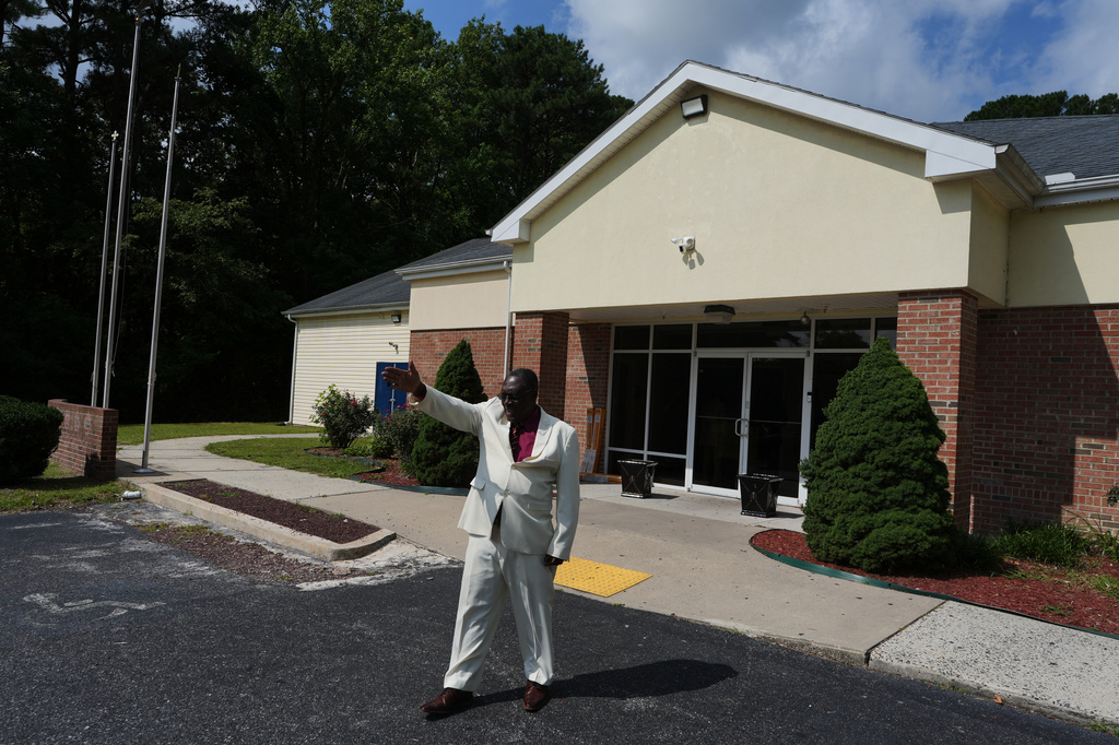 Roosevelt Toussaint, the senior pastor of the Word of Life Center church, points to empty parking spaces outside his church before a service, which he says is due to fear in the Haitian community of possible arrests and deportation in Salisbury, Md., Sunday, Aug. 2, 2026. (AP Photo/Luis Andres Henao)