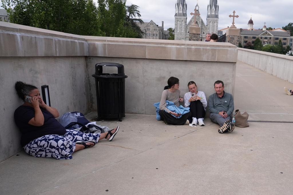 CORECTS TO PEOPLE, NOT POLICE - People shelter behind a wall on the Villanova University campus in Villanova, Pa., on Thursday, Aug. 21, 2025, where an active shooter was reported. (AP Photo/Matt Slocum)