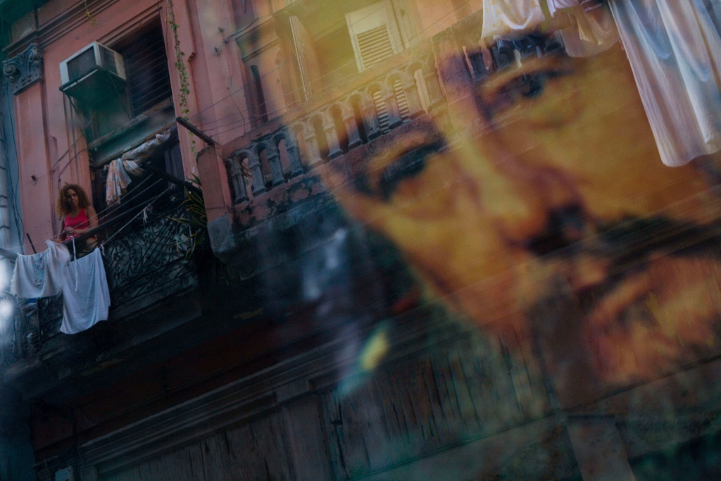 FILE - A Cuban woman hanging laundry on her balcony is seen reflected in a glass window decorated with a poster of Cuba's leader Fidel Castro in Old Havana, Cuba, Thursday, Dec. 27, 2007. (AP Photo/Dado Galdieri, File)