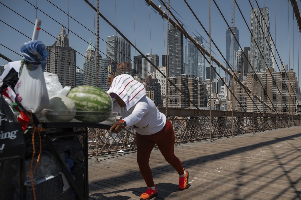 FILE - A fruit vendor pushes her cart on the Brooklyn Bridge during a heat wave on June 24, 2025, in New York. (AP Photo/Olga Fedorova, File)