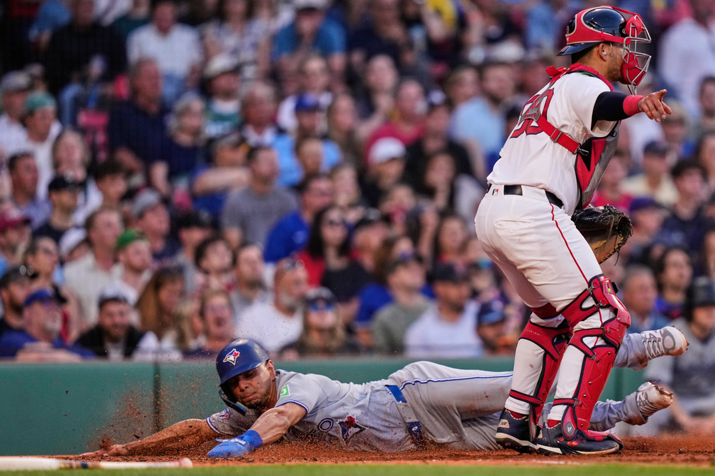 Toronto Blue Jays' Andrés Giménez, left, scores on a ground out by Vladimir Guerrero Jr., as Boston Red Sox catcher Mickey Gasper signals the throw to go to first, during the third inning of a baseball game, Wednesday, June 17, 2026, in Boston. (AP Photo/Charles Krupa)