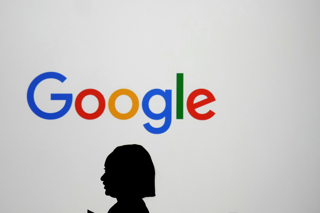 FILE - A woman walks by a giant screen with a logo at an event at the Paris Google Lab on the sidelines of the AI Action Summit in Paris, Feb. 9, 2025. (AP Photo/Thibault Camus, File)
