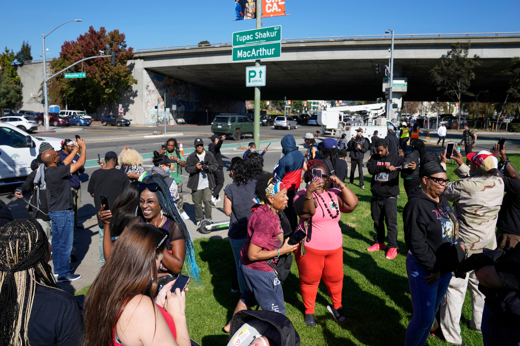 FILE - People take pictures and gather beneath a new sign during a street renaming ceremony for Tupac Shakur in Oakland, Calif., Nov. 3, 2023. (AP Photo/Eric Risberg, File)