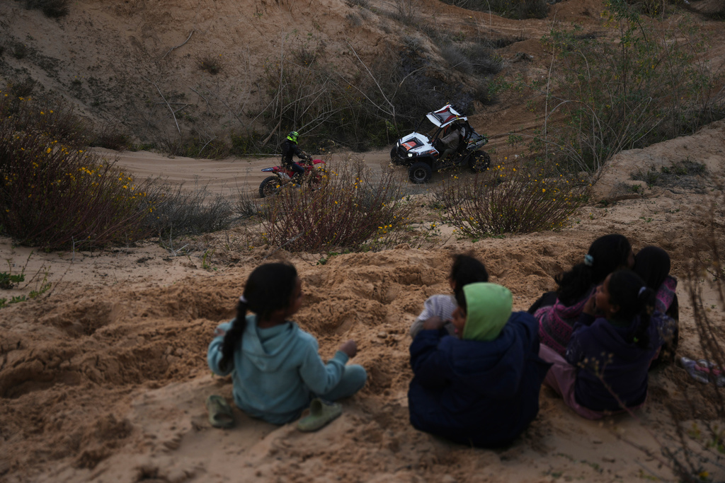 Palestinians watch youths riding their motorcycles and ATV on sand dunes in the Al-Zahra area, in the central Gaza Strip, Friday, Dec. 5, 2025. (AP Photo/Abdel Kareem Hana)