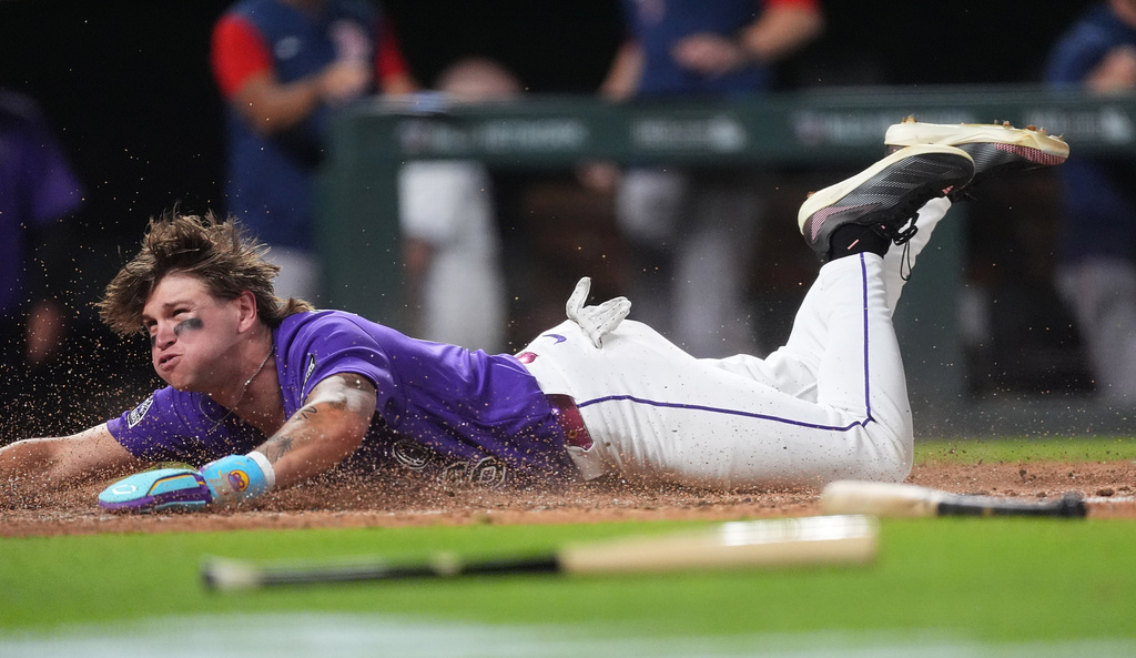 Colorado Rockies' Cole Carrigg dives into home plate to score the winning run on a three-run walkoff triple hit by Jake McCarthy off Boston Red Sox relief pitcher Aroldis Chapman in the ninth inning of a baseball game Monday, June 22, 2026, in Denver. (AP Photo/David Zalubowski)