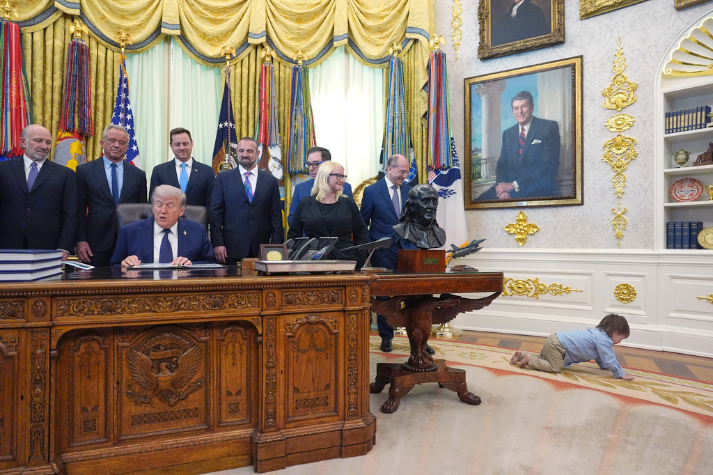 Travis Smith, 2, crawls on the floor as President Donald Trump speaks during an event on health care affordability in the Oval Office at the White House, Thursday, April 23, 2026, in Washington. (AP Photo/Mark Schiefelbein)