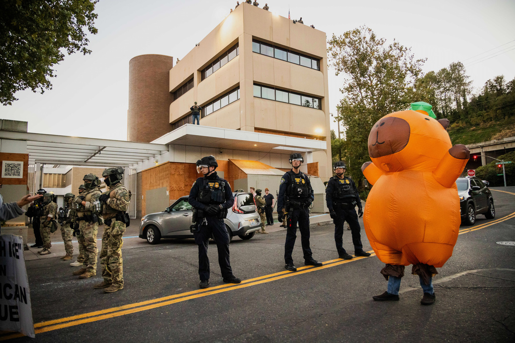 A protester in costume walk past police and federal agents during a protest near a U.S. Immigration and Customs Enforcement facility in Portland, Ore., Monday, Oct. 6, 2025. (AP Photo/Ethan Swope)