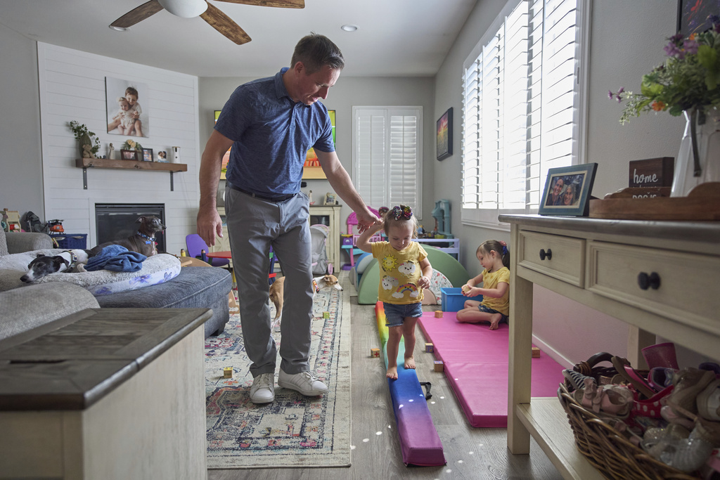 Josh Marris holds the hand of his daughter, Brooklyn Marris, as she walks on a balance board as her sister, Alana, right, plays at their home in Winchester, Calif., on Thursday, Sept. 18, 2025. (AP Photo/Gregory Bull)