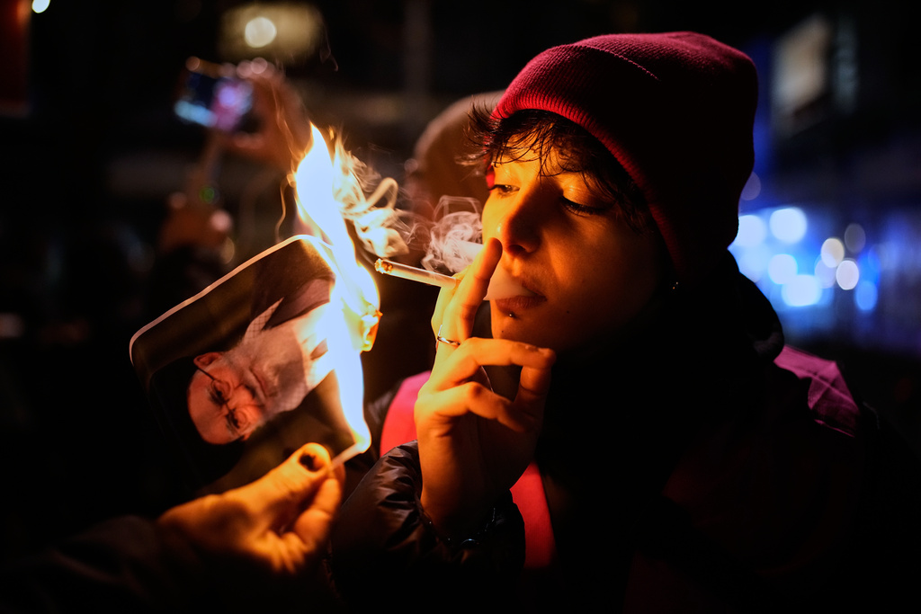 FILE - A protester smokes a cigarette after lighting it off a burning poster of Iran's Supreme Leader Ayatollah Ali Khamenei in Berlin, Germany, Jan. 14, 2026, in support of the nationwide mass protests in Iran against the government. (AP Photo/Ebrahim Noroozi, File)