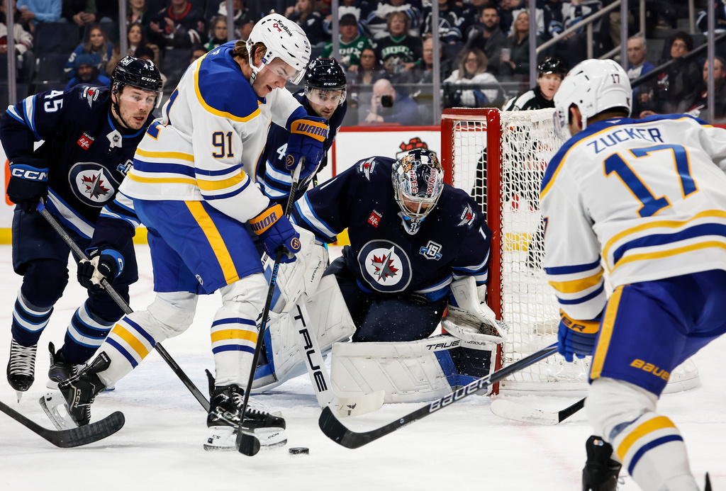 Winnipeg Jets goaltender Eric Comrie (1) keeps his eye on the rebound as Buffalo Sabres' Josh Doan (91) tries to knock it in during first period NHL action in Winnipeg on Friday, Dec. 5, 2025. (John Woods/The Canadian Press via AP)