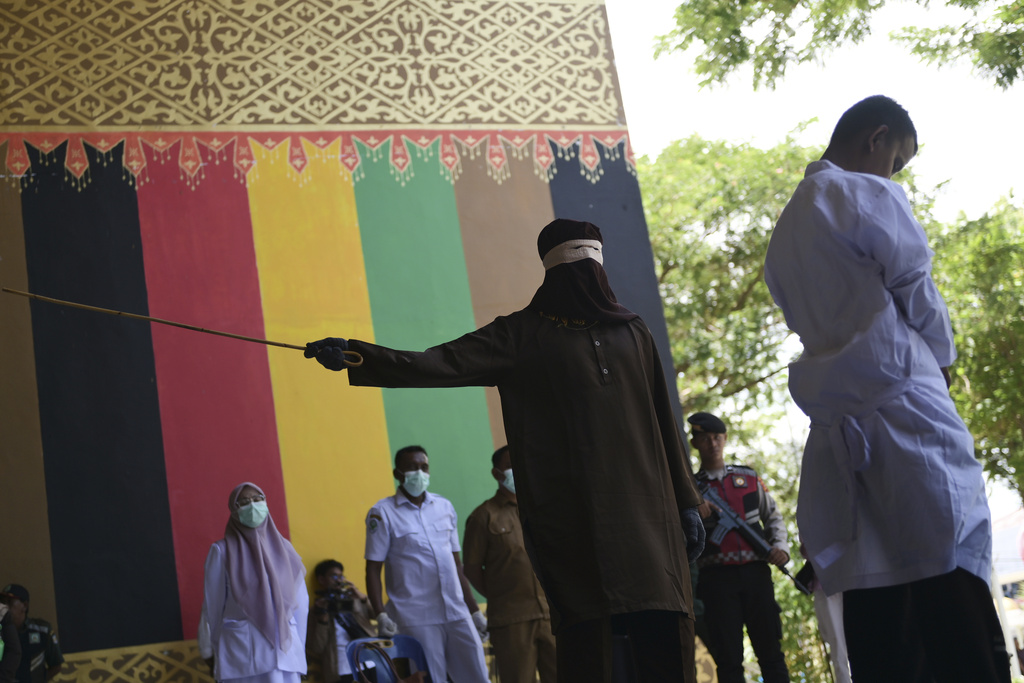 An official uses a rattan cane to whip one of two men convicted of violating Islamic law by hugging and kissing, which the court ruled can lead to banned sexual relations, in Banda Aceh, Aceh province, Indonesia, Tuesday, Aug. 26, 2025. (AP Photo/Reza Saifullah)