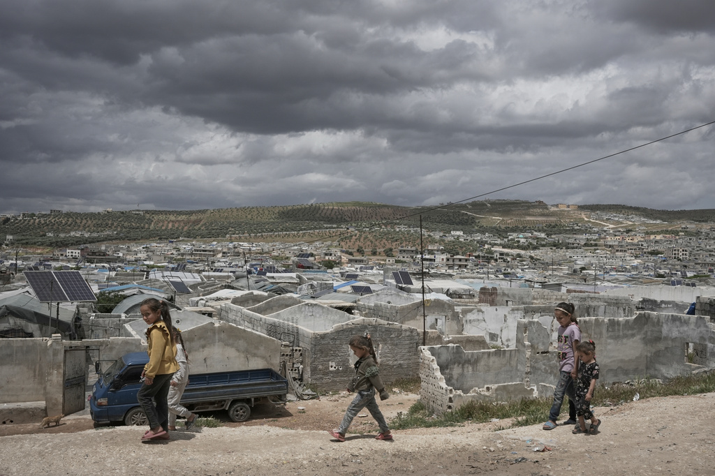 Syrian children walk along a dirt path at the edge of al-Karama camp, built from scratch with light-brick structures covered with fabric and housing internally displaced Syrians near the village of Atmeh, Idlib province, Syria, Tuesday, May 19, 2026. (AP Photo/Omar Albam)