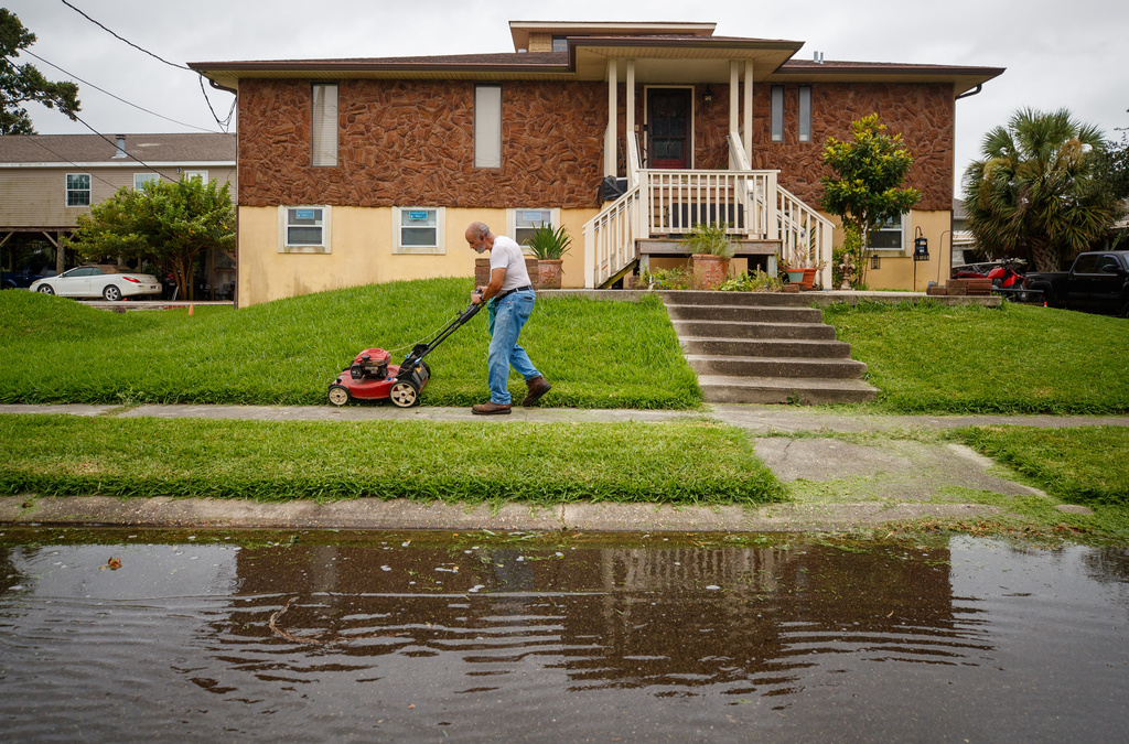 Clarence Hebert, 69, mows his lawn as winds from Tropical Storm Bertha push water into the street just after the morning high tide in Venetian Isles, La., Wednesday, July 22, 2026. (David Grunfeld/The Times-Picayune/The New Orleans Advocate via AP)