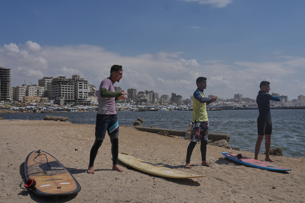 Palestinians Tahseen Abu Assi, left, Khalil Abu Jayyab, center, and Abed Rahim Alostaz warm up before surfing on the beach in Gaza City, Monday, May 4, 2026. (AP Photo/Jehad Alshrafi)