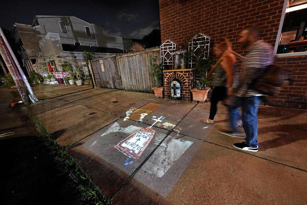 This photo of a makeshift tomb at a New Orleans street corner, concealing a body that had been lying on the sidewalk for days in the wake of Hurricane Katrina, taken by AP photographer Dave Martin, is projected onto the same sidewalk Tuesday, Aug. 19, 2025, in New Orleans. (AP Photo/Gerald Herbert)