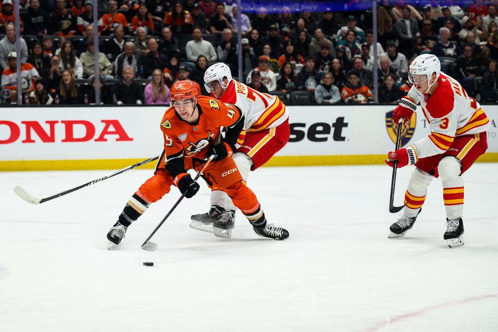 Anaheim Ducks right wing Beckett Sennecke (45) tries to keep control of the puck while under pressure from Calgary Flames center Martin Pospisil, center, during the first period of an NHL hockey game Saturday, April 4, 2026, in Anaheim, Calif. (AP Photo/William Liang)