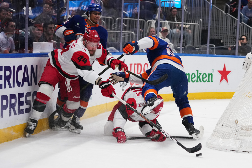Carolina Hurricanes' Nicolas Deslauriers (44) and Skyler Brind'amour (76) fights for control of the puck with New York Islanders' Isaiah George (36) and Scott Mayfield (24) during the first period of an NHL hockey game Tuesday, April 14, 2026, in Elmont, N.Y. (AP Photo/Frank Franklin II)
