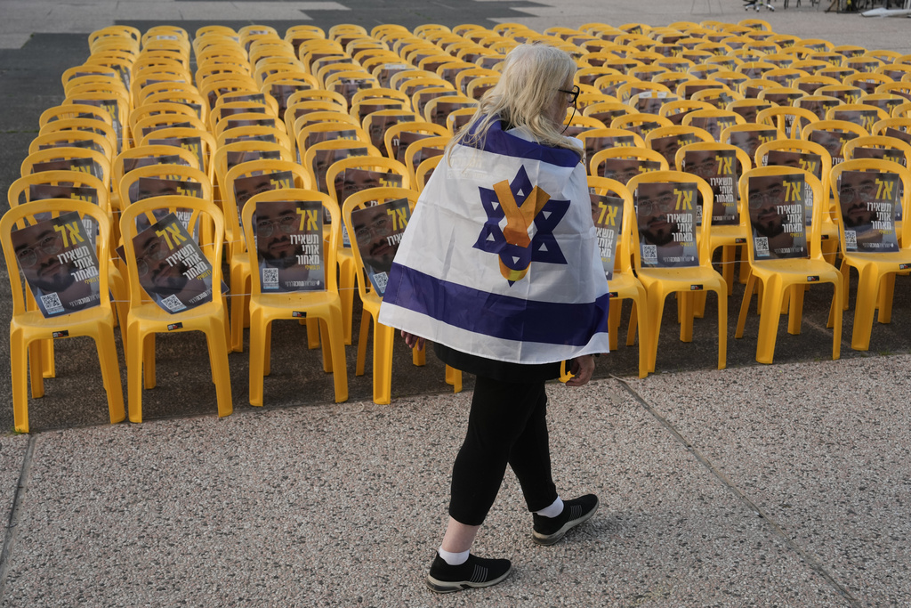 A woman walks by chairs with photos of Ran Gvili, the final hostage in Gaza who was killed while fighting Hamas militants during the Oct. 7, 2023 attack and whose remains have been recovered Monday, clearing the way for the next phase of the ceasefire that paused the Israel-Hamas war, in a plaza known as Hostages Square in Tel Aviv, Israel, Monday, Jan. 26, 2026. (AP Photo/Oded Balilty)