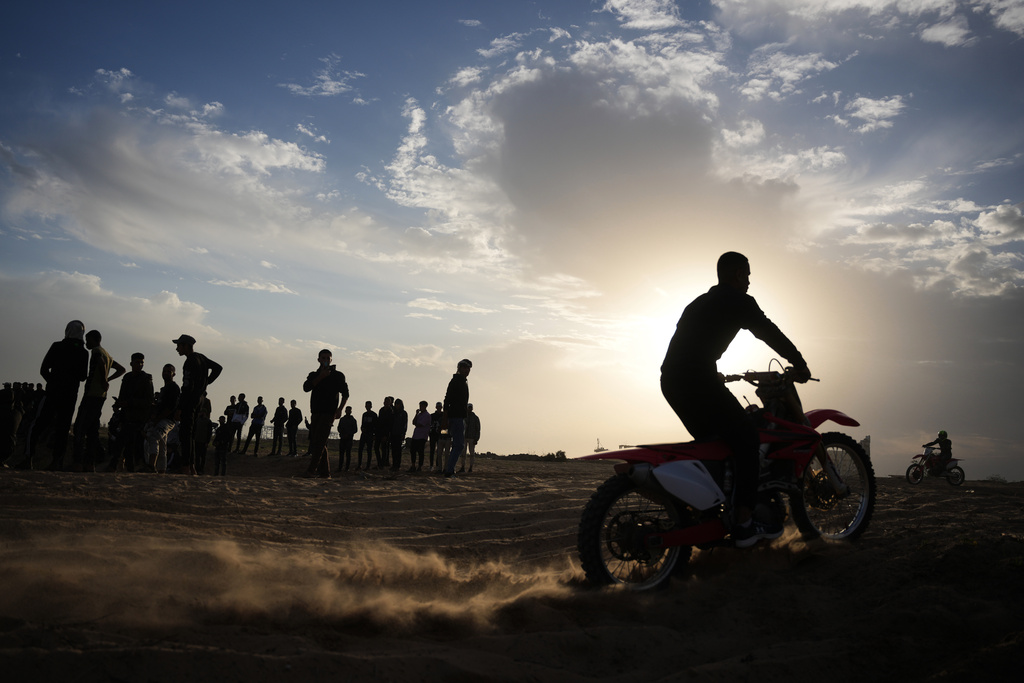 Palestinians watch youths riding their motorcycles on a sand dune in the Al-Zahra area, in the central Gaza Strip, Friday, Dec. 5, 2025. (AP Photo/Abdel Kareem Hana)
