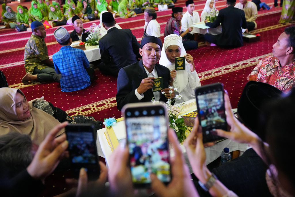 A bride and groom show their wedding certificates after getting married as family members use their mobile phones to take photos during a mass wedding ceremony at Istiqlal Mosque in Jakarta, Indonesia, Wednesday, Dec. 3, 2025. (AP Photo/Tatan Syuflana)