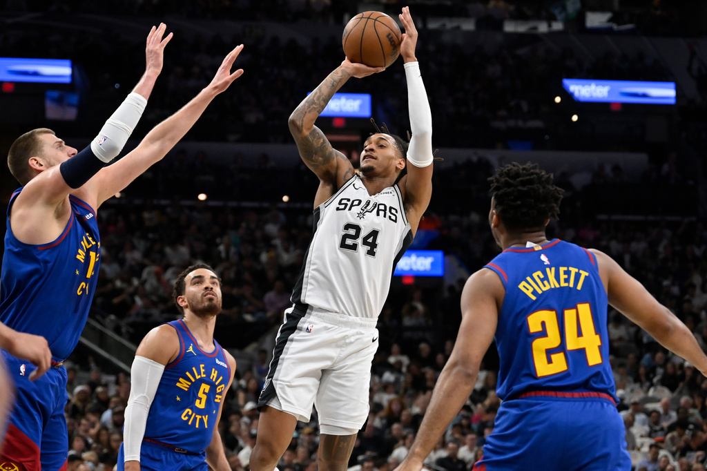 San Antonio Spurs guard Devin Vassell shoots against Denver Nuggets' Nikola Jokic, left, Tyus Jones (5) and Jalen Pickett, right, during the first half of an NBA basketball game, Sunday, April 12, 2026, in San Antonio. (AP Photo/Darren Abate)