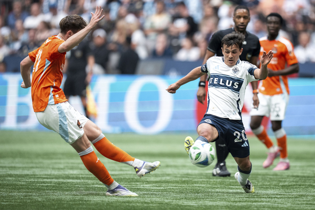 Houston Dynamo's Jack McGlynn kicks the ball as Vancouver Whitecaps' Andres Cubas (20) defends during the first half of an MLS soccer match in Vancouver, British Columbia, Sunday, Aug. 17, 2025. (Ethan Cairns/The Canadian Press via AP)