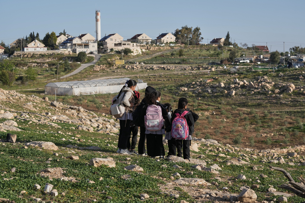 Palestinian students walk to school using an alternative route that is nearly twice as long because a fence separates their village from the nearby Israeli settlement of Carmel, near the West Bank village of Umm al-Khair, Tuesday, April 14, 2026. (AP Photo/Mahmoud Illean)
