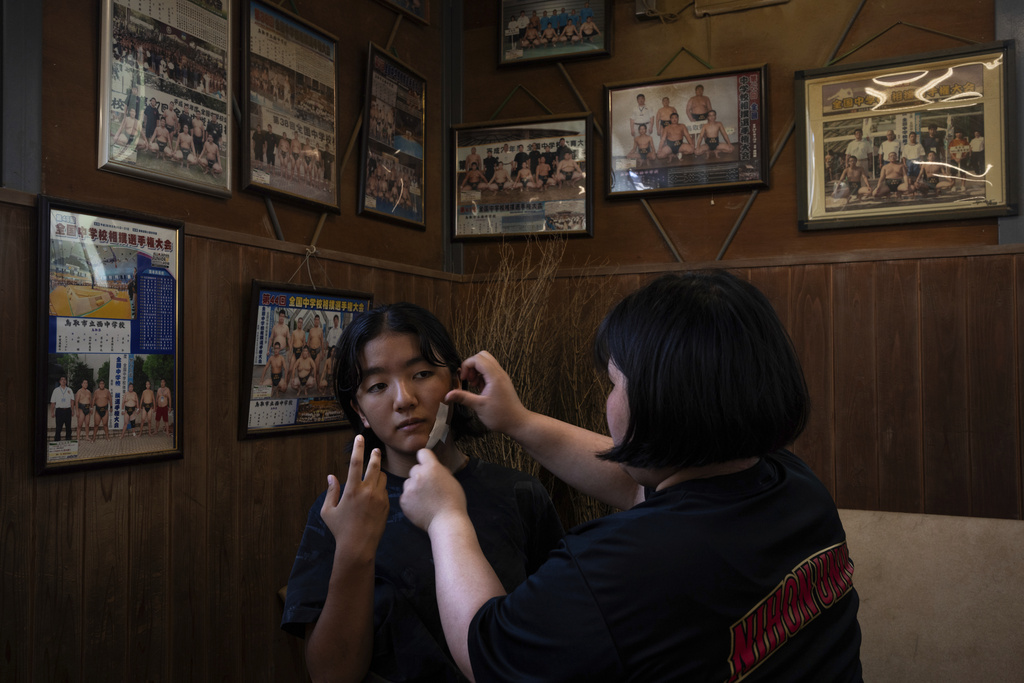 Straps are applied to a wrestler's face as pictures of male wrestlers are hung on the wall prior to a practice session at a sumo camp in Tottori Johoku High School in Tottori, Japan, on July 28, 2025. (AP Photo/Louise Delmotte)