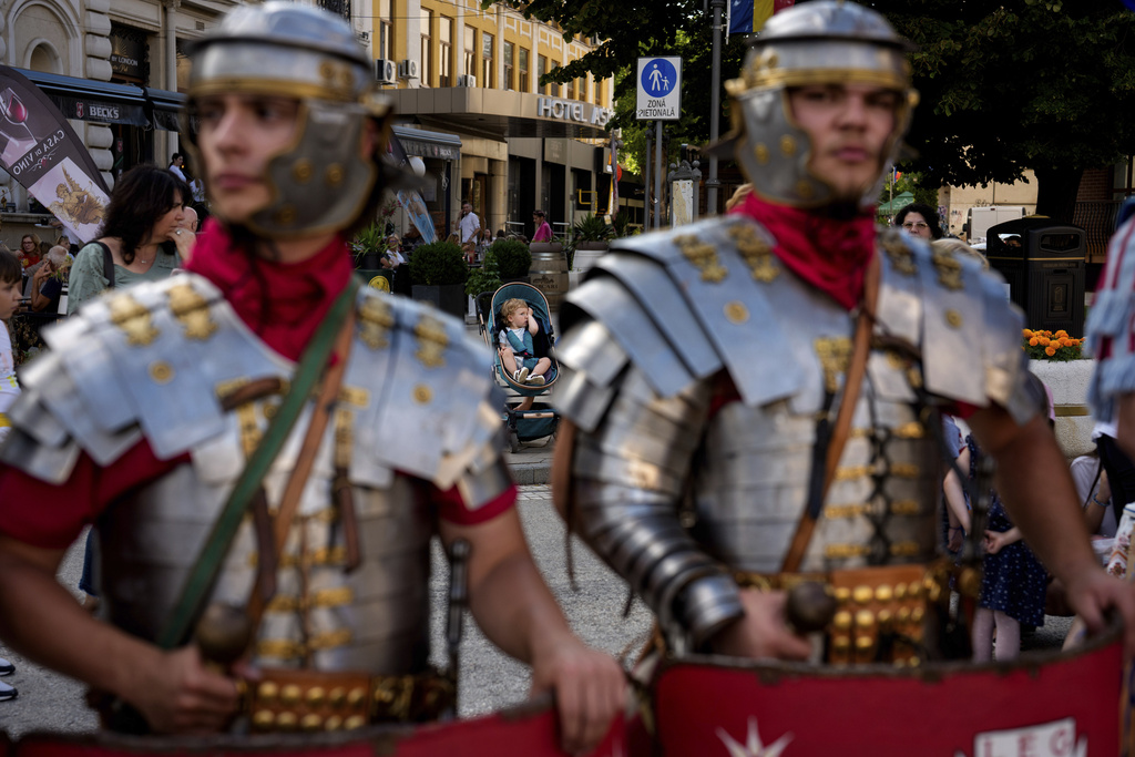 A baby sits in a stroller behind men wearing Roman soldiers outfits in Iasi, Romania, Friday, July 11, 2025 ahead of the Getodava historical reenactment festival. (AP Photo/Andreea Alexandru)